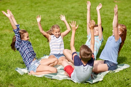friendship, childhood, leisure and people concept - group of happy kids or friends sitting and having fun on grass in summer parkの写真素材