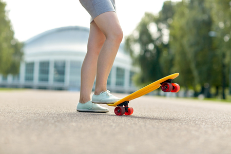 skateboarding, leisure, extreme sport and people concept - close up of teenage girl legs riding short modern cruiser skateboard on roadの写真素材