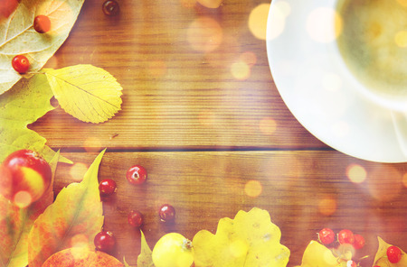 season, drink and morning concept - close up of coffee cup on wooden table with autumn leaves