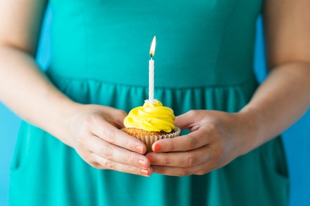 holiday, celebration, people, greeting and party concept - close up of woman with burning candle on birthday cupcakeの写真素材