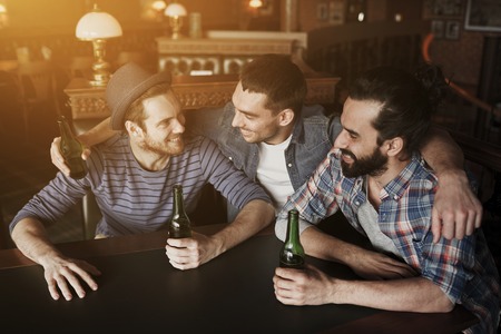 people, leisure, friendship and bachelor party concept - happy male friends drinking bottled beer and hugging at bar or pubの写真素材