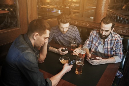 people, men, leisure, friendship and communication concept - male friends with smartphones drinking...