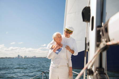 sailing, age, tourism, travel and people concept - happy senior couple hugging on sail boat or yacht deck floating in seaの写真素材