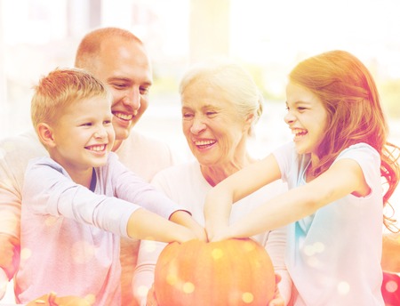 family, happiness, generation, holidays and people concept - happy family making halloween pumpkins at homeの写真素材