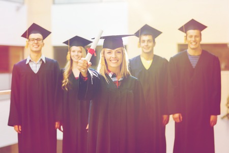 education, graduation and people concept - group of smiling students in mortarboards and gowns with diploma outdoorsの写真素材