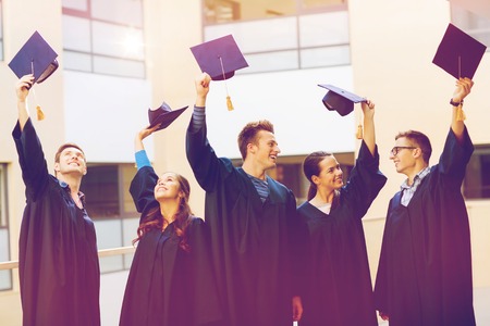 education, graduation and people concept - group of smiling students in gowns waving mortarboards outdoorsの写真素材