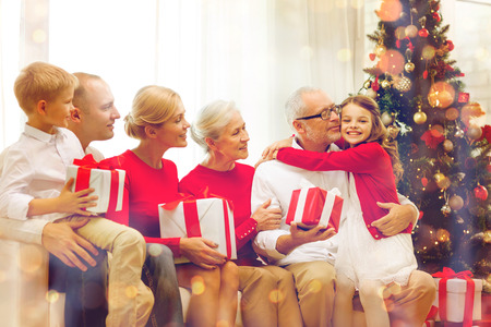 family, holidays, generation, christmas and people concept - smiling family with gift boxes sitting on couch at homeの写真素材