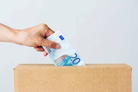charity, finances, funding, investment and people concept - male hand putting euro money into donation boxの写真素材