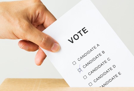 voting, civil rights and people concept - close up of male hand putting vote into ballot box on...