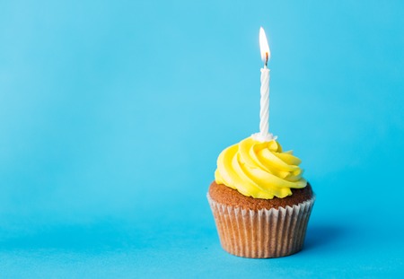 holiday, celebration, greeting and party concept - birthday cupcake with one burning candle over blue backgroundの写真素材