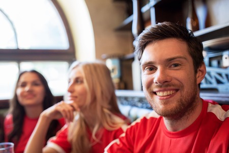 people, leisure and sport concept - happy friends or football fans drinking beer and watching soccer game or match at bar or pubの写真素材