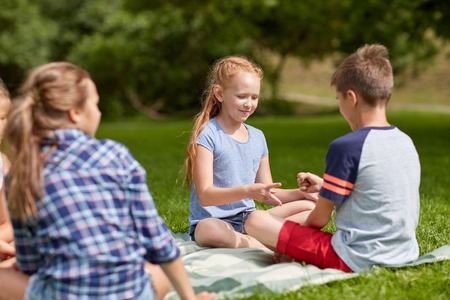 summer holidays, entertainment, childhood, leisure and people concept - group of happy pre-teen kids playing rock-paper-scissors game in parkの写真素材