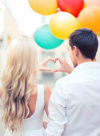 summer holidays, celebration and dating concept - couple with colorful balloons making heart shape in the cityの写真素材