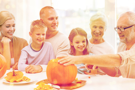 family, happiness, generation, holidays and people concept - happy family making halloween pumpkins...