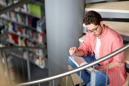education, high school, university, learning and people concept - student boy or young man reading...