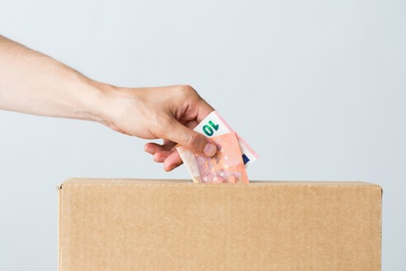 charity, finances, funding, investment and people concept - male hand putting euro money into donation boxの写真素材