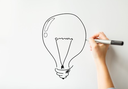 idea, inspiration, business, people and education concept - close up of hand with marker drawing light bulb on white board or wallの写真素材
