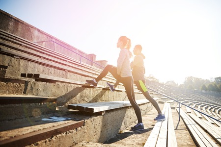 fitness, sport, exercising and lifestyle concept - couple stretching leg on stands of stadiumの写真素材