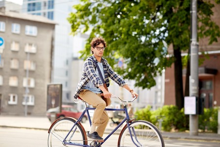 people, style, leisure and lifestyle - young hipster man with shoulder bag riding fixed gear bike on city streetの写真素材