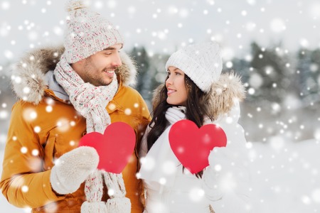 people, season, love and valentines day concept - happy couple holding blank red hearts over winter landscapeの写真素材