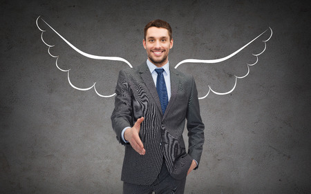 business, angel investor, safety, security and people concept - smiling young businessman with wings drawing giving hand for handshake over gray concrete background