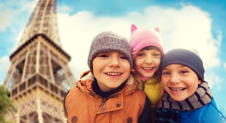 childhood, tourism, travel, vacation and people concept - group of happy kids over eiffel tower and sky backgroundの写真素材