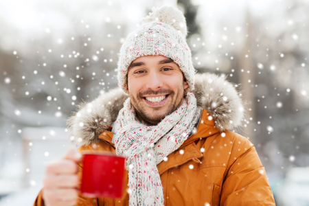 people, season, drinks and leisure concept - happy man with tea cup outdoors in winterの写真素材