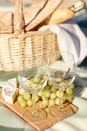 food, holidays and celebration  concept - close up of picnic basket with grapes, wine glasses, cheese and champagne bottle on summer beachの写真素材