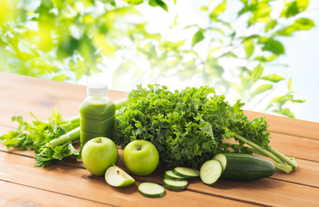 healthy eating, food, dieting and vegetarian concept - bottle with green juice, fruits and vegetables on wooden table over green natural backgroundの写真素材