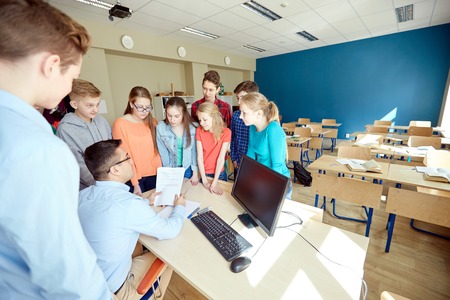 education, school, learning, teaching and people concept - group of students and teacher talking in...