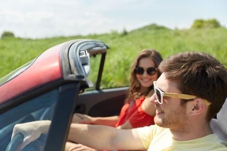 leisure, road trip, travel, summer holidays and people concept - happy couple driving in cabriolet...