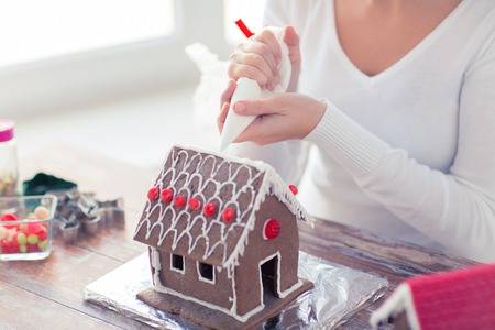 cooking, people, christmas and decoration concept - close up of happy woman making gingerbread houses at homeの写真素材