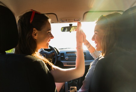 summer vacation, holidays, travel, road trip and people concept - happy teenage girls or young women driving in car and making high five gestureの写真素材