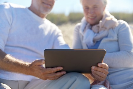 family, age, travel, technology and people concept - close up of senior couple with tablet pc computer sitting on deck chairs on summer beachの写真素材