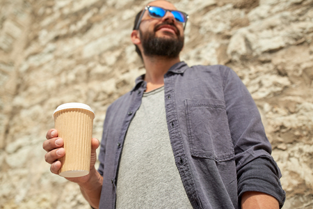 people, drinks, leisure and lifestyle concept - close up of man drinking coffee from disposable paper cup on city streetの写真素材