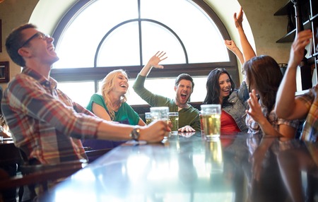people, leisure, friendship and entertainment concept - happy friends drinking beer, watching sport game or football match and celebrating victory at bar or pubの写真素材