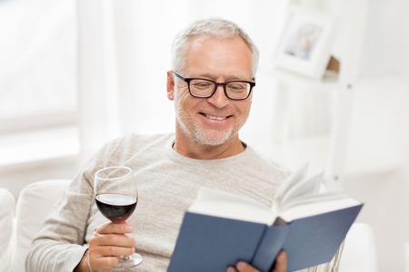 age, leisure and people concept - happy smiling senior man with wine glass reading book at homeの写真素材