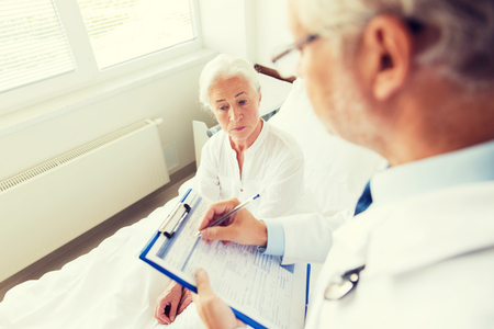 medicine, age, health care and people concept - senior woman and doctor writing to clipboard at hospital wardの写真素材