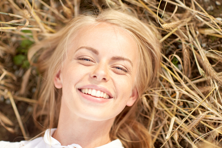 nature, summer holidays, vacation and people concept - happy smiling young woman or teenage girl lying and enjoying sun on cereal fieldの写真素材