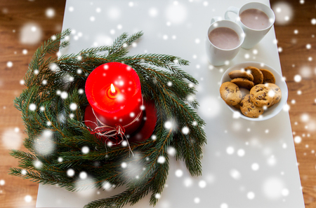 christmas, holidays, winter and still life concept - close up of fir wreath with burning candle, oat cookies and cups with hot chocolate or cocoa drink on table at homeの写真素材