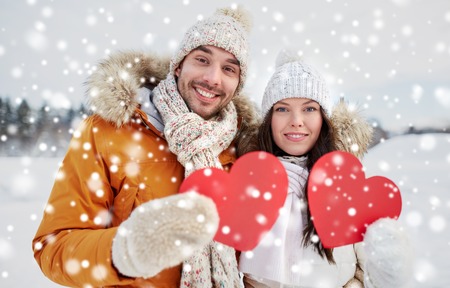 people, season, love and valentines day concept - happy couple holding blank red hearts over winter landscapeの写真素材