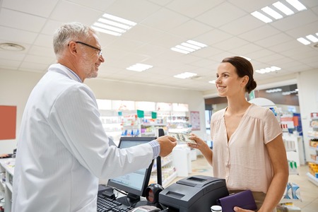 medicine, pharmaceutics, health care and people concept - smiling woman with wallet giving money to senior man pharmacist at drugstore cash registerの写真素材