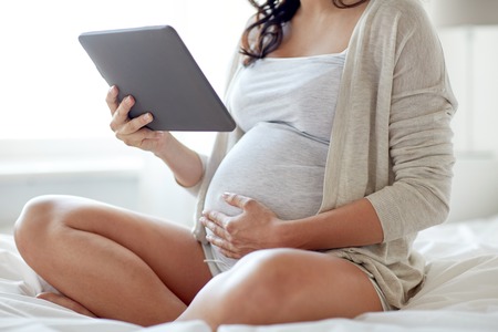 pregnancy, technology, people and expectation concept - close up of pregnant woman with tablet pc computer in bed at homeの写真素材