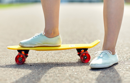 skateboarding, leisure, extreme sport and people concept - close up of teenage girl legs riding short modern cruiser skateboard on roadの写真素材