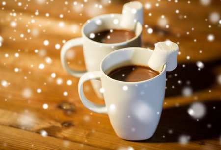 holidays, winter, food and drinks concept - close up of cups with hot chocolate or cocoa drinks and marshmallow on wooden tableの写真素材