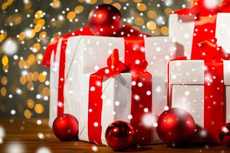 christmas, holidays, presents, new year and celebration concept - close up of gift boxes and red balls on wooden floor over lights backgroundの写真素材