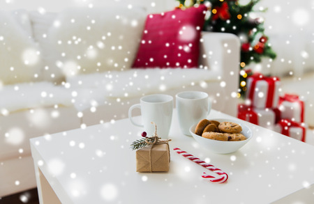 christmas, holidays and  winter concept - close up of gift, oat cookies, sugar cane candy and cups on table at homeの写真素材
