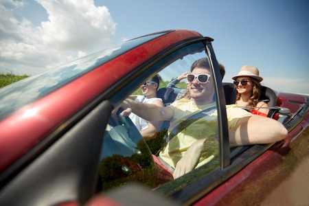 leisure, road trip, travel and people concept - happy friends driving in cabriolet car along country...