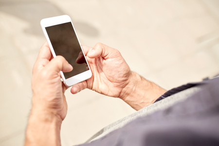 leisure, technology, communication and people concept - close up of man with smartphone on streetの写真素材