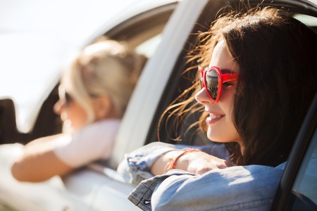 summer holidays, valentines day, travel, road trip and people concept - happy teenage girls or young women heart shaped sunglasses in car at seasideの写真素材